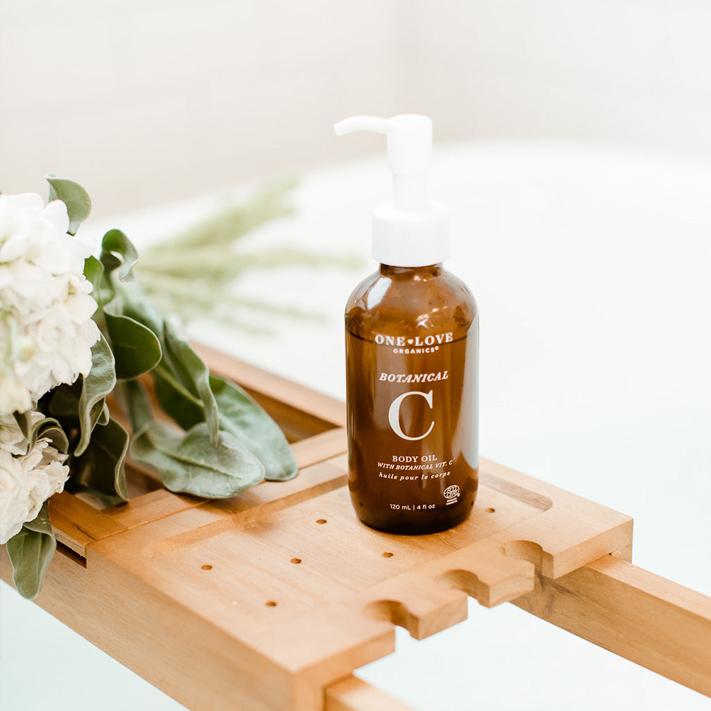 A bottle of one love botanical c body oil on a wooden tray next to a bouquet of flowers.