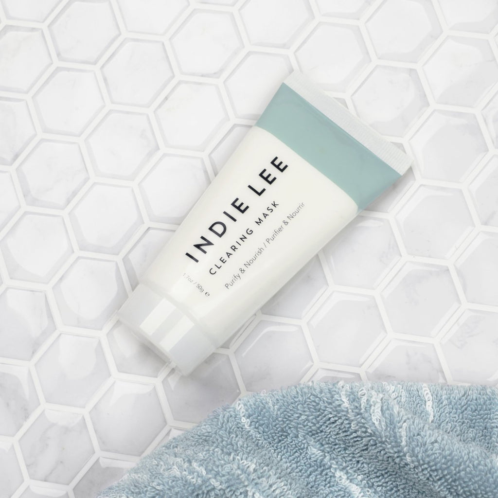 Indie lee clearing mask product on a hexagonal tiled surface next to a blue towel.