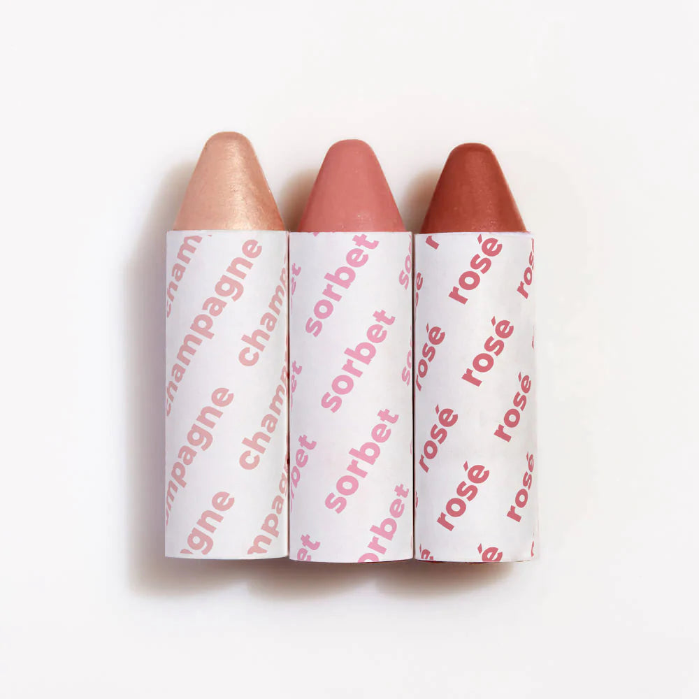Three lip crayons with shades labeled champagne, sorbet, and rose, displayed side by side against a white background.