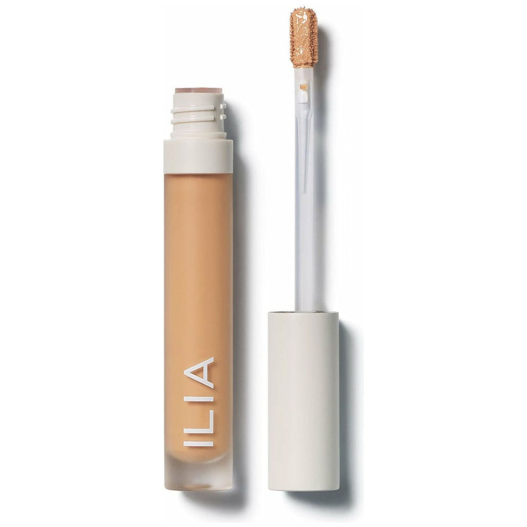 A bottle of ilia brand liquid concealer with its applicator wand removed and resting on the surface.