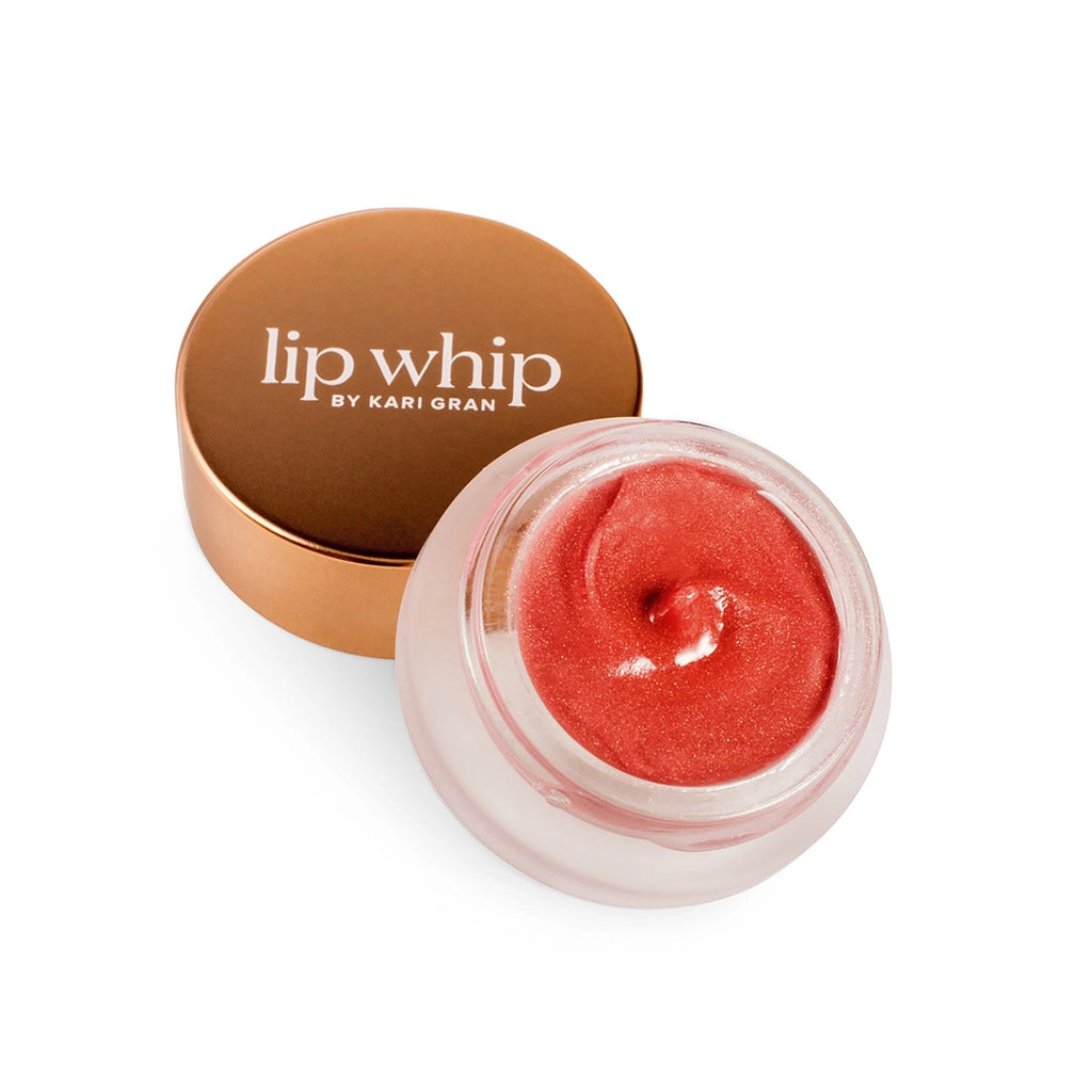 A jar of red-tinted lip whip next to its bronze lid on a white background.