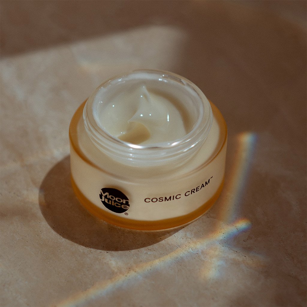 Open jar of facial cream with a soft texture, branded "cosmic cream," bathed in natural light with a rainbow spectrum reflection.