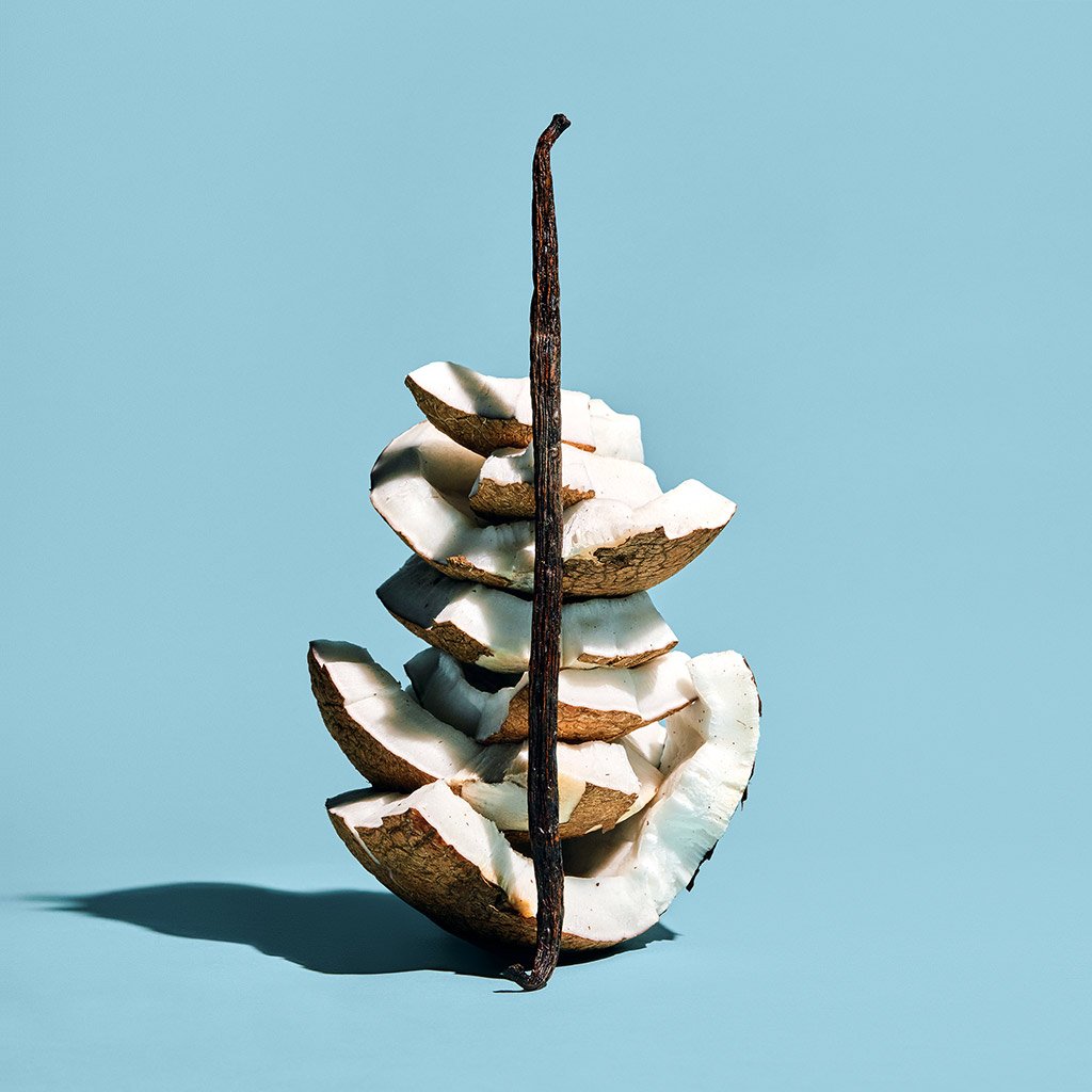 Sliced coconut in mid-air against a blue background, arranged to appear whole with the husk intact.