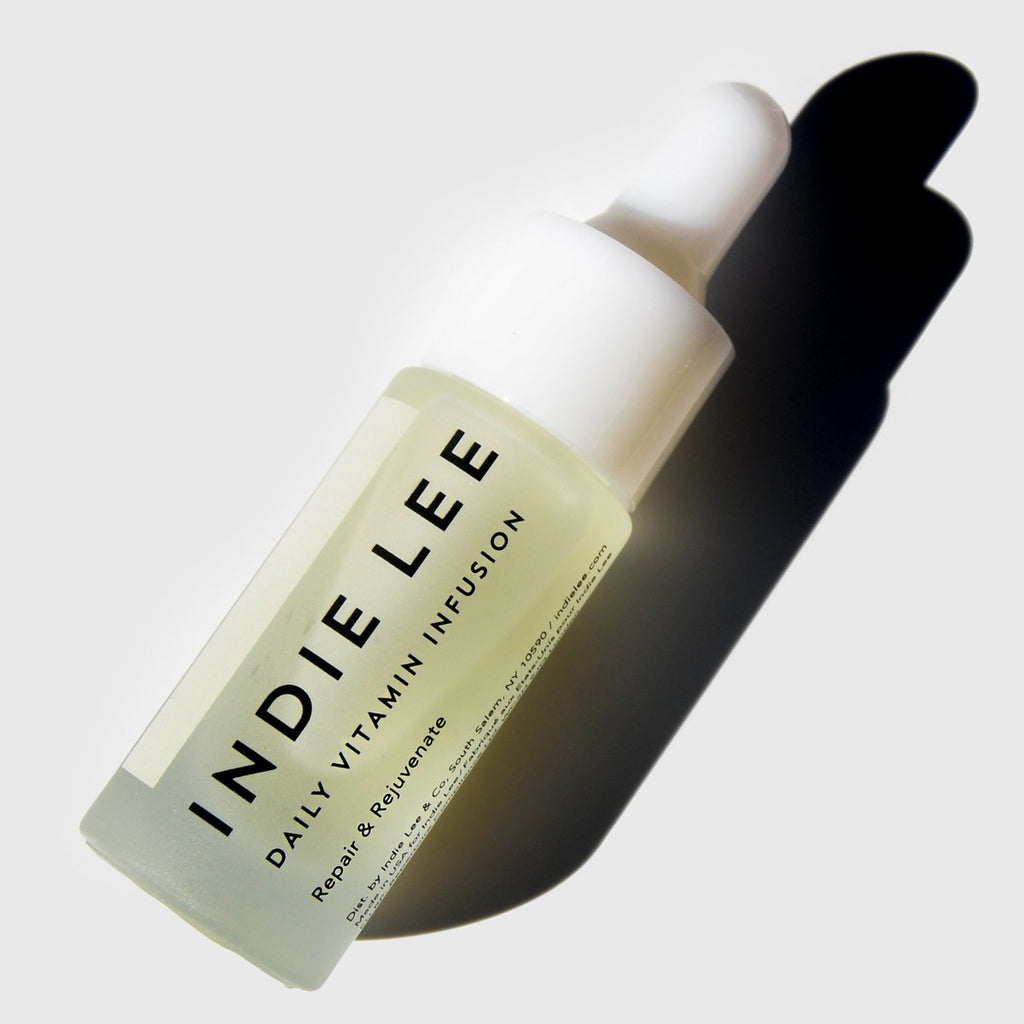 A bottle of indie lee daily vitamin infusion with a dropper cap, casting a shadow on a light background.