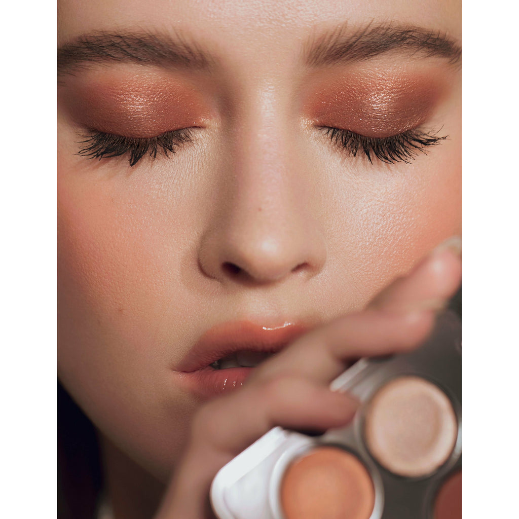 Close-up of a person applying eyeshadow with autumnal shades.