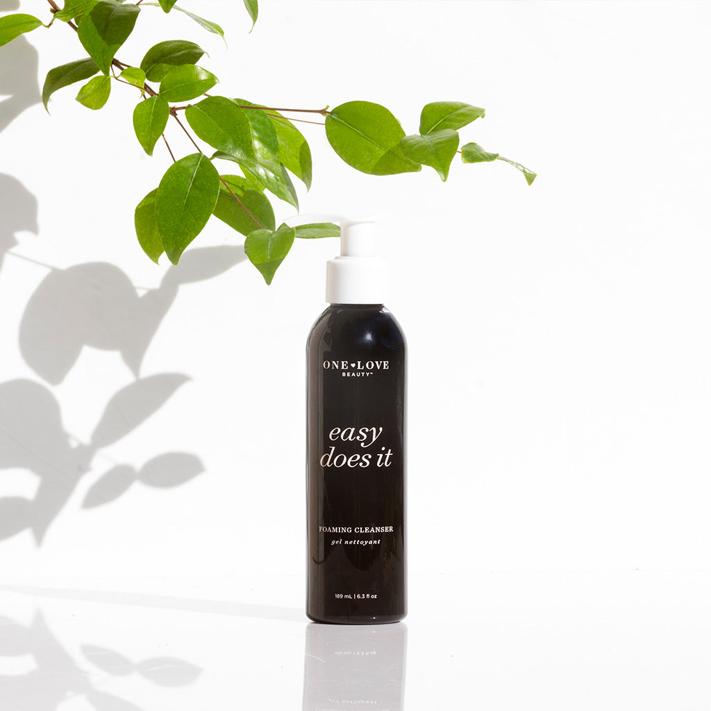 A bottle of one love organics foaming cleanser on a white surface with plant shadows.