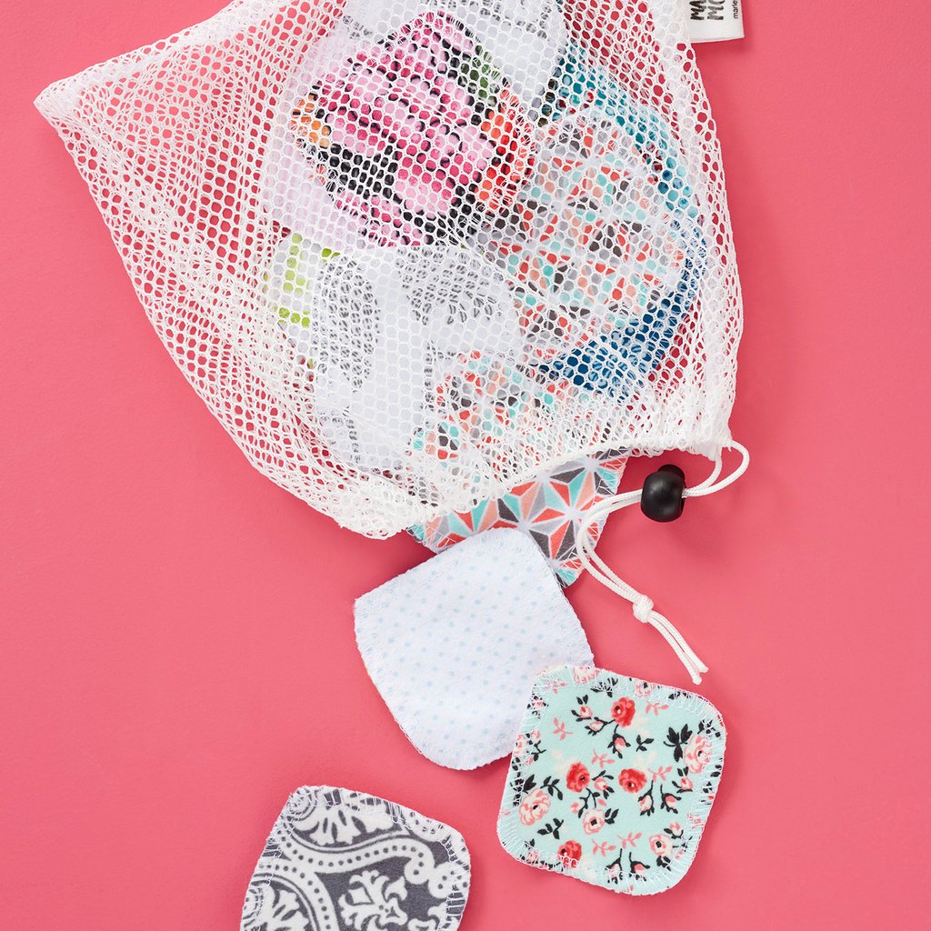 A reusable mesh laundry bag with a collection of fabric menstrual pads spilling out onto a pink surface.