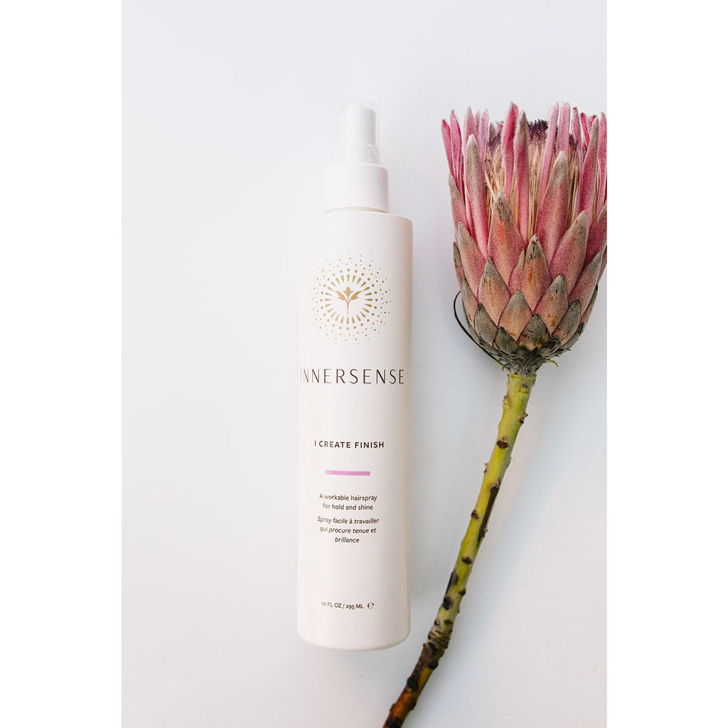 A bottle of innersense brand product next to a dried pink protea flower against a white background.