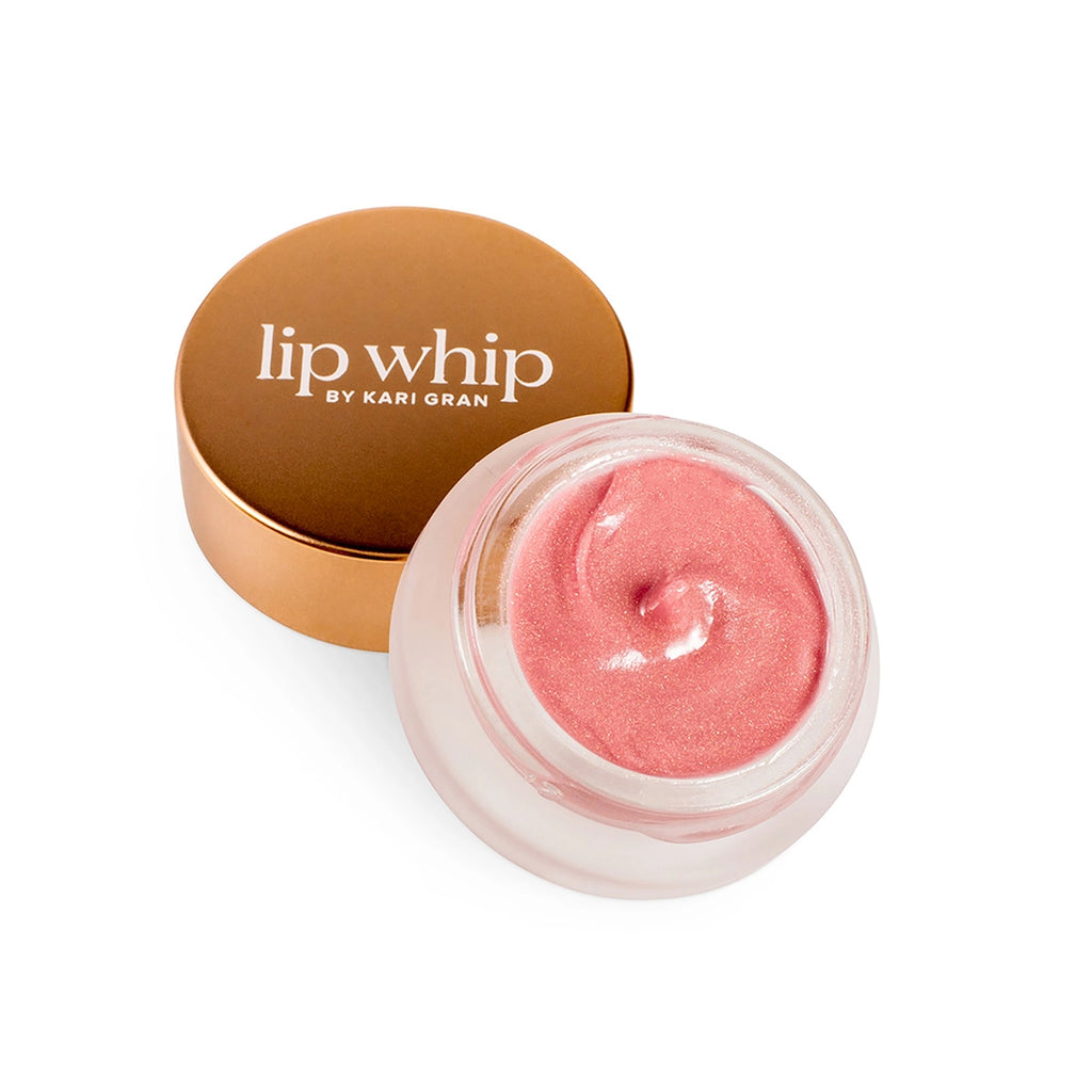 Lip whip by kari gran: a pink tinted lip balm presented in an open glass jar with a metallic gold-colored lid set beside it on a white background.