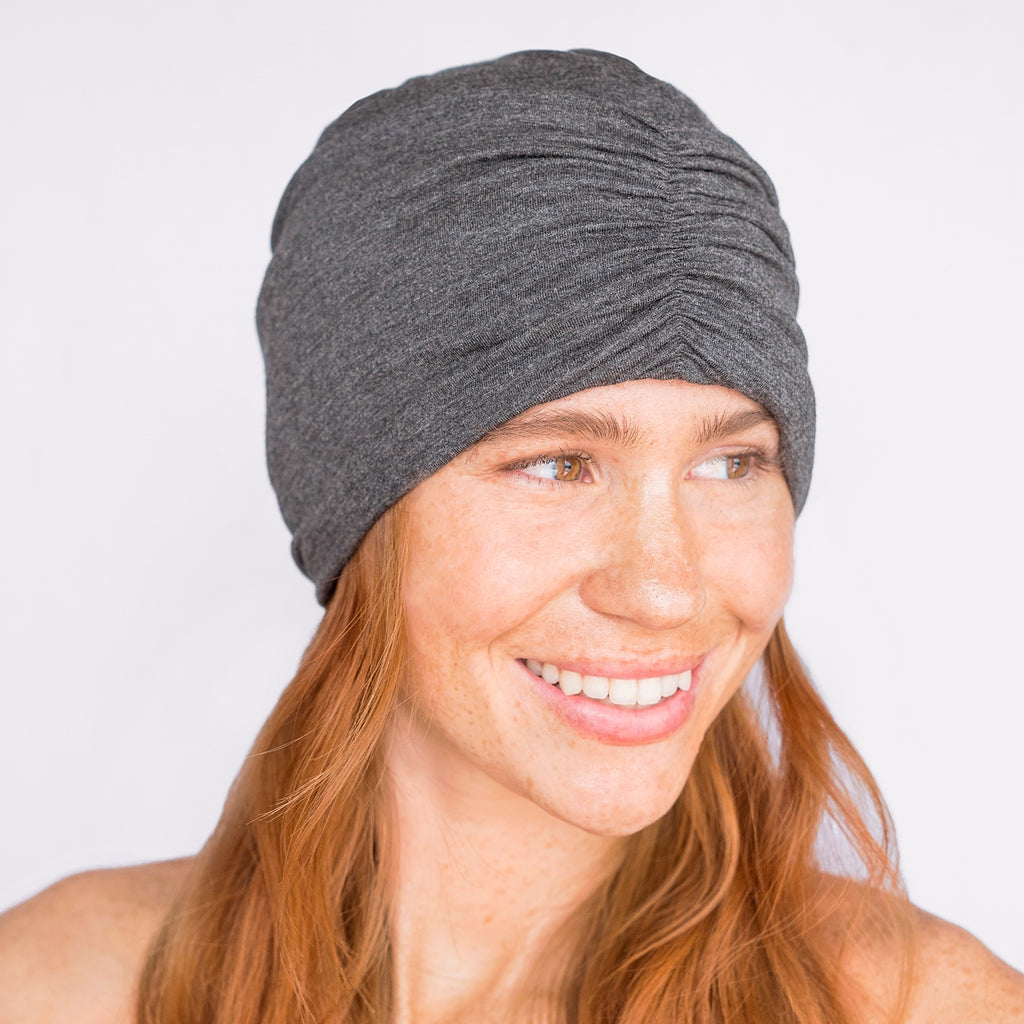 Woman smiling while wearing a gray headwrap.