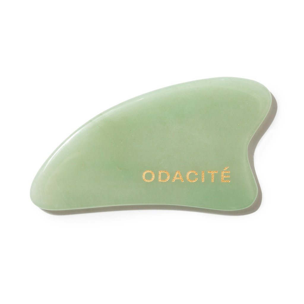 A green jade facial gua sha tool with the brand name "odacite" printed on it.