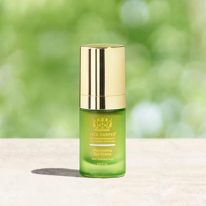 A bottle of tata harper illuminating eye cream with diamond dust on a blurred natural background.