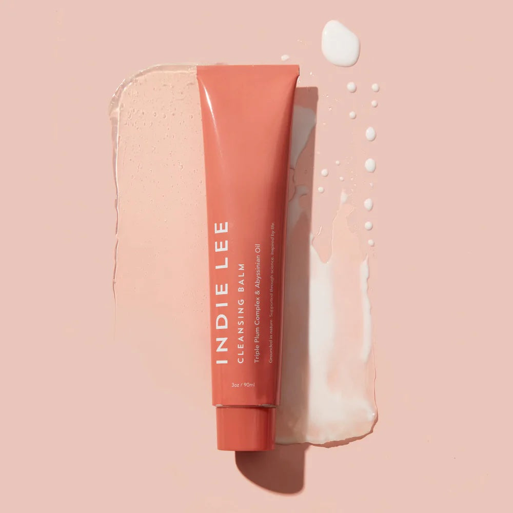 A tube of indie lee cleansing balm with a swatch of the product against a pastel background.
