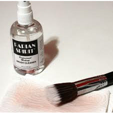 A bottle of brush cleaner and a makeup brush with pink bristles on a white surface.