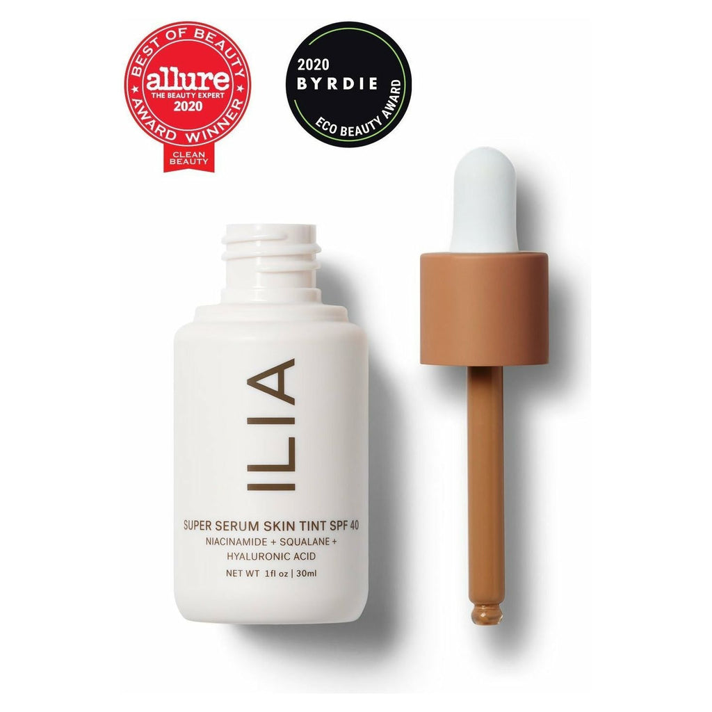 A bottle of ilia super serum skin tint spf 40 next to its dropper applicator, displaying awards from allure and byrdie for beauty excellence.