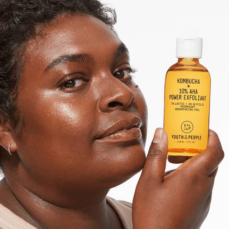 Woman holding a bottle of kombucha aha exfoliant next to her face.
