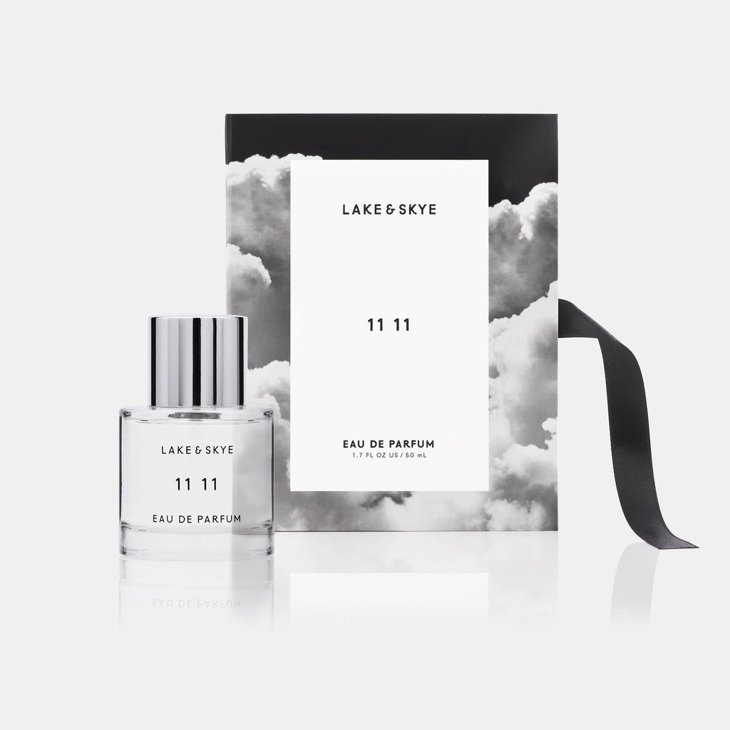 Bottle of lake & skye 11 11 eau de parfum with packaging against a cloud-themed backdrop.