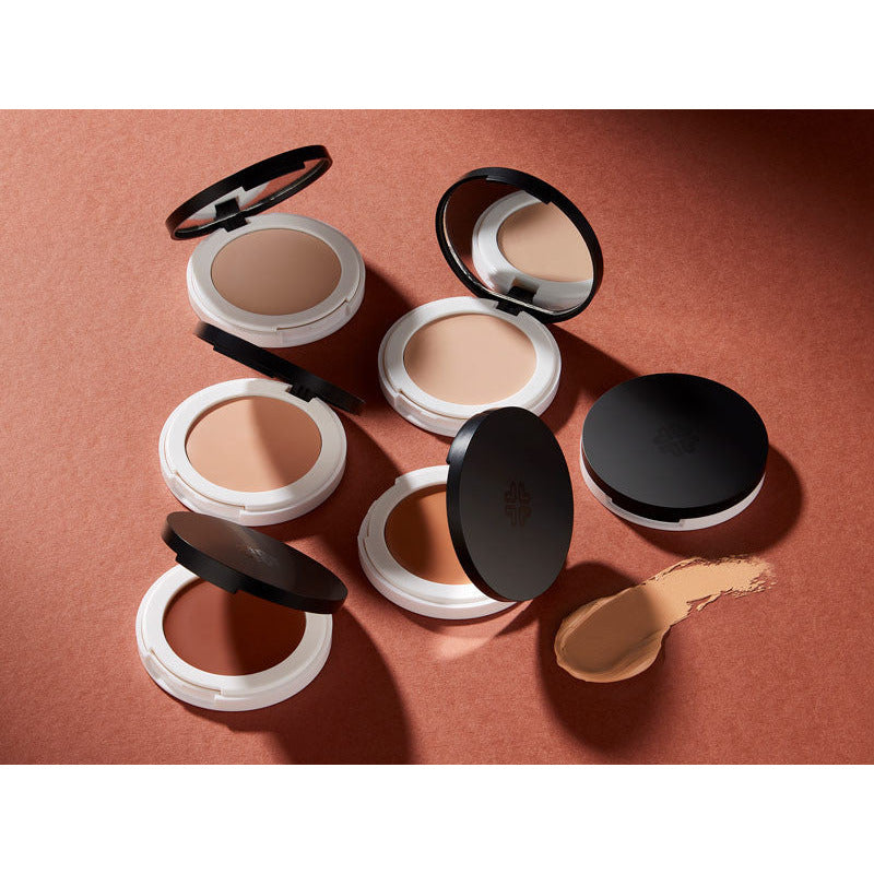 Assorted makeup compacts with foundation in various shades on a coral background.