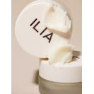 A jar of ilia brand cream with its lid propped against it, showing the creamy texture of the product inside.