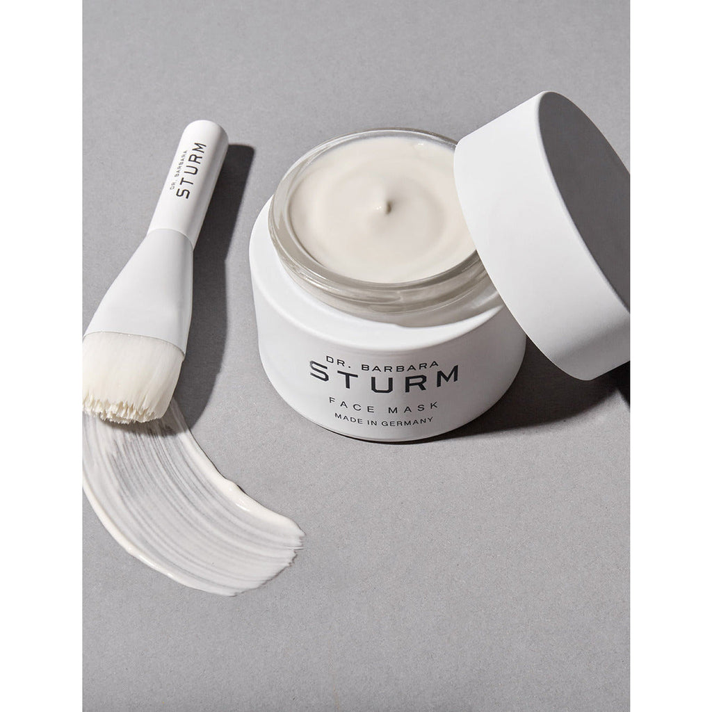 A jar of dr. barbara sturm face mask with an application brush on a grey surface.