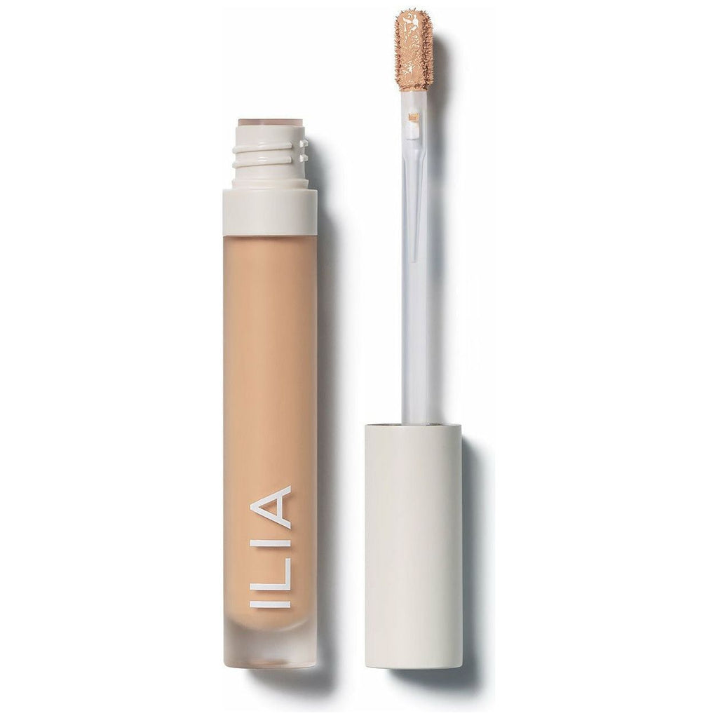 A bottle of ilia concealer with its applicator wand displayed beside the open container.