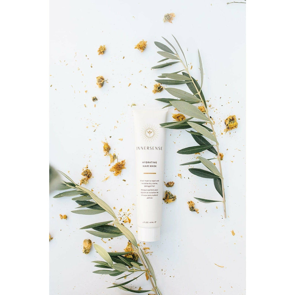 Cosmetic product surrounded by eucalyptus leaves and yellow flowers on a light background.
