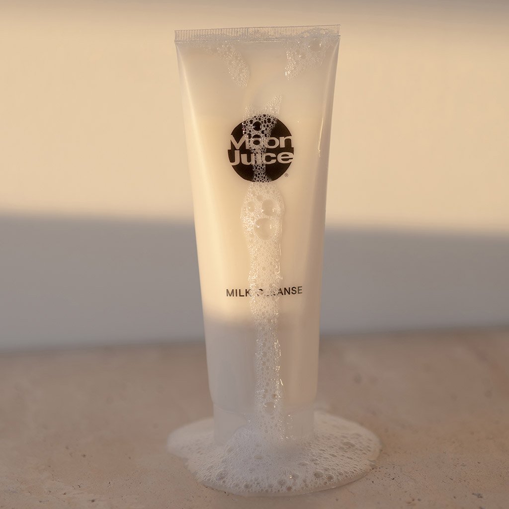 A tube of "moon juice" brand cleanser overflowing with product against a neutral background.