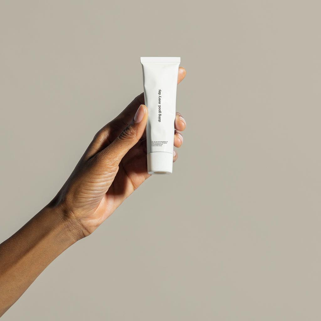 A hand holding a tube of skincare product against a neutral background.