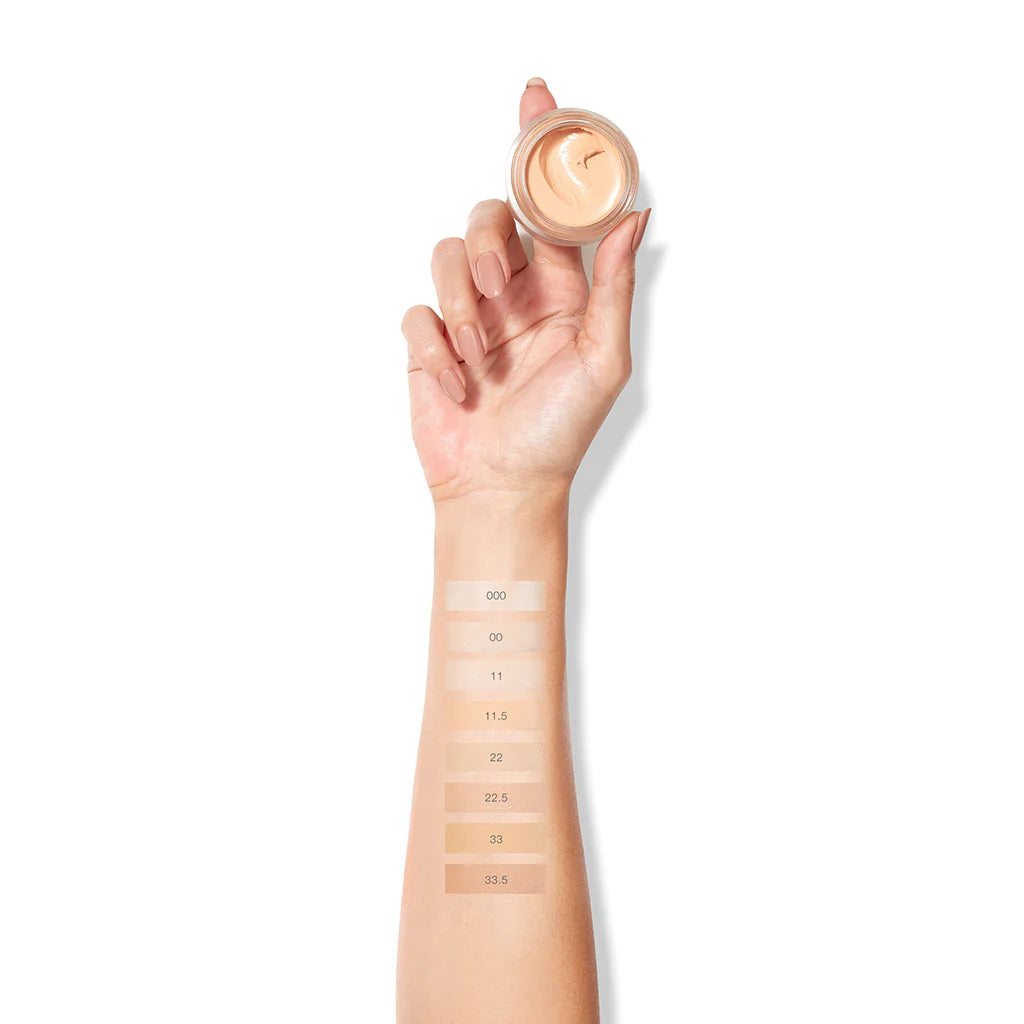 Foundation shades swatched on forearm with open container of product in hand.