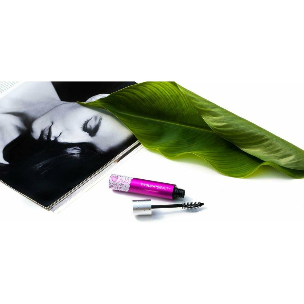 Open magazine with a monochrome portrait near a green leaf and pink mascara on a white background.