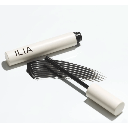 An open tube of ilia mascara with its brush lying next to it.