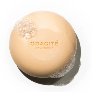 A beige-colored odacite skincare product with suds on a white background.