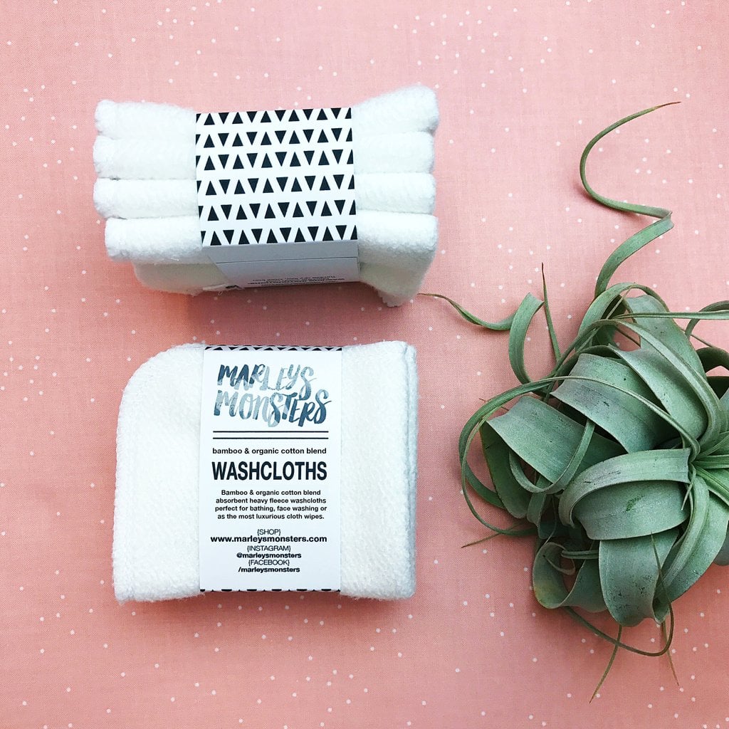 Two packs of bamboo cotton blend washcloths on a pink surface next to a green plant.