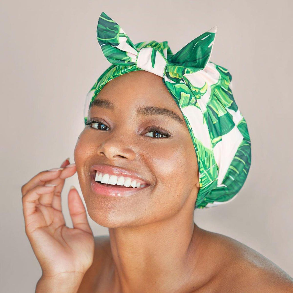 A smiling woman with a green and white headwrap touching her face.