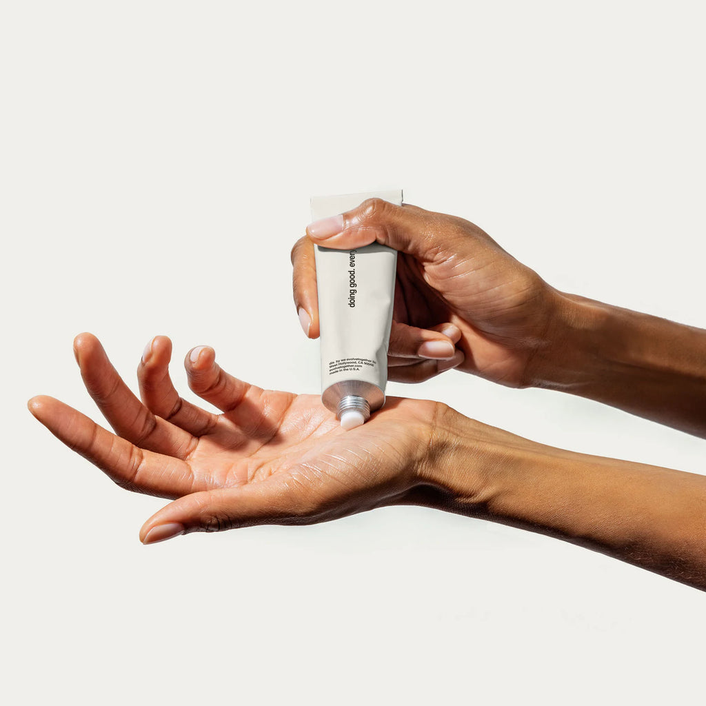A person dispensing lotion from a tube onto their hand.