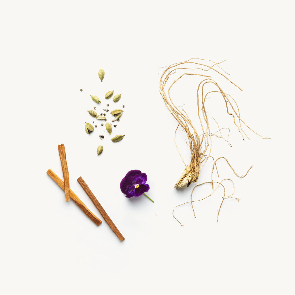 Various botanical items, including cinnamon sticks, cardamom pods, a purple flower, and dried roots, arranged neatly on a white background.