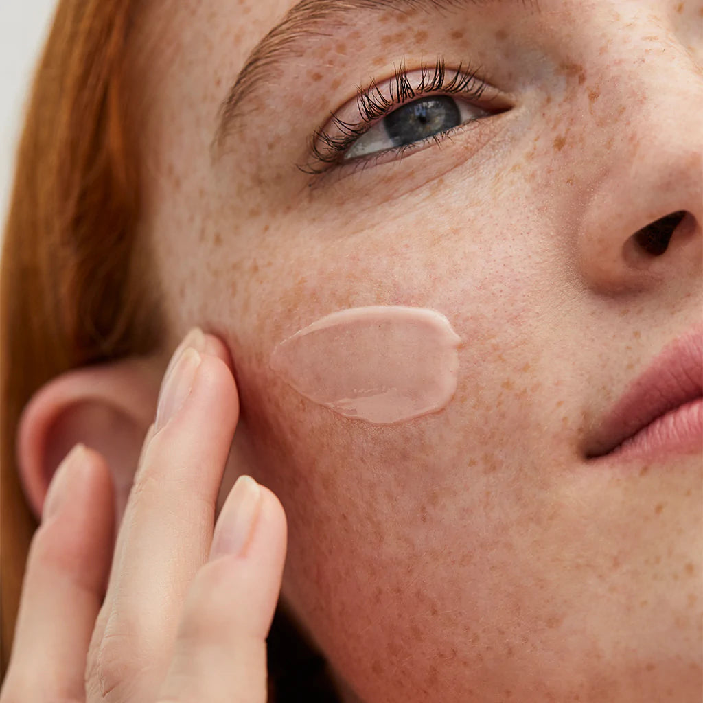 Person applying skincare cream on their cheek.