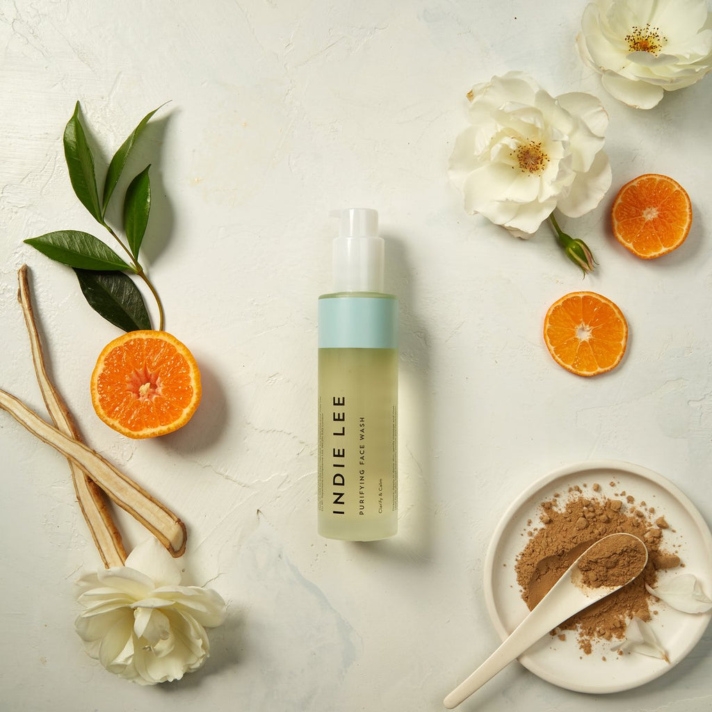 Cosmetic product display with citrus and flowers on a neutral background.