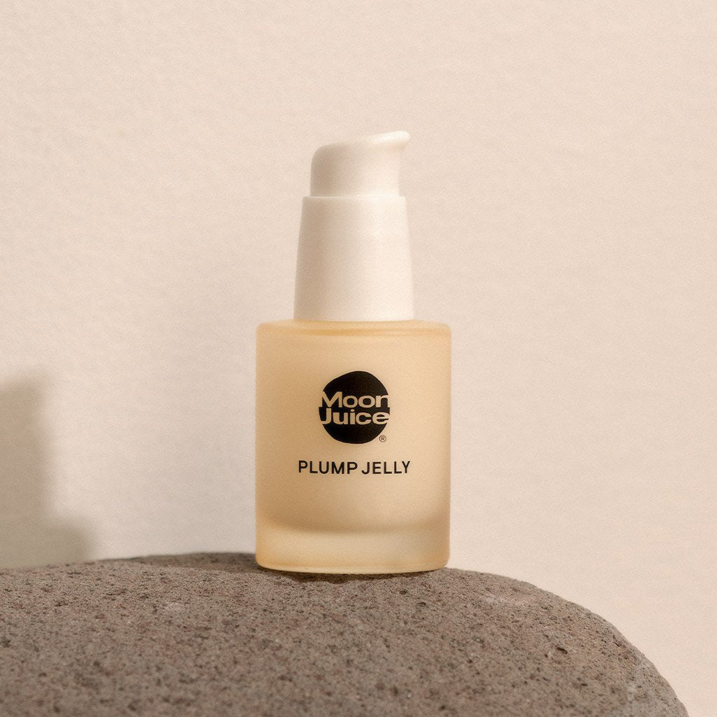 A bottle of "moon juice plump jelly" skincare product resting on a textured stone surface against a neutral backdrop.