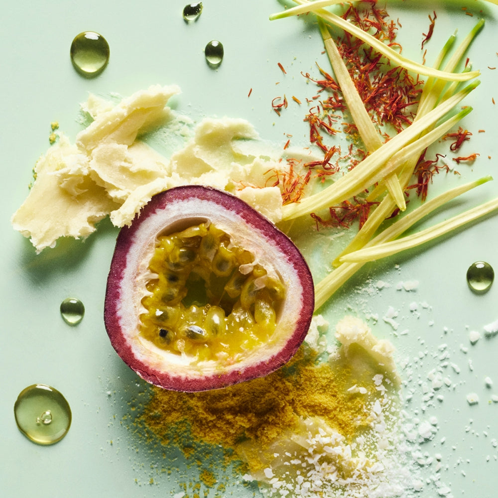 Halved passion fruit with seeds, scattered saffron threads, and assorted spices on a pastel green surface.