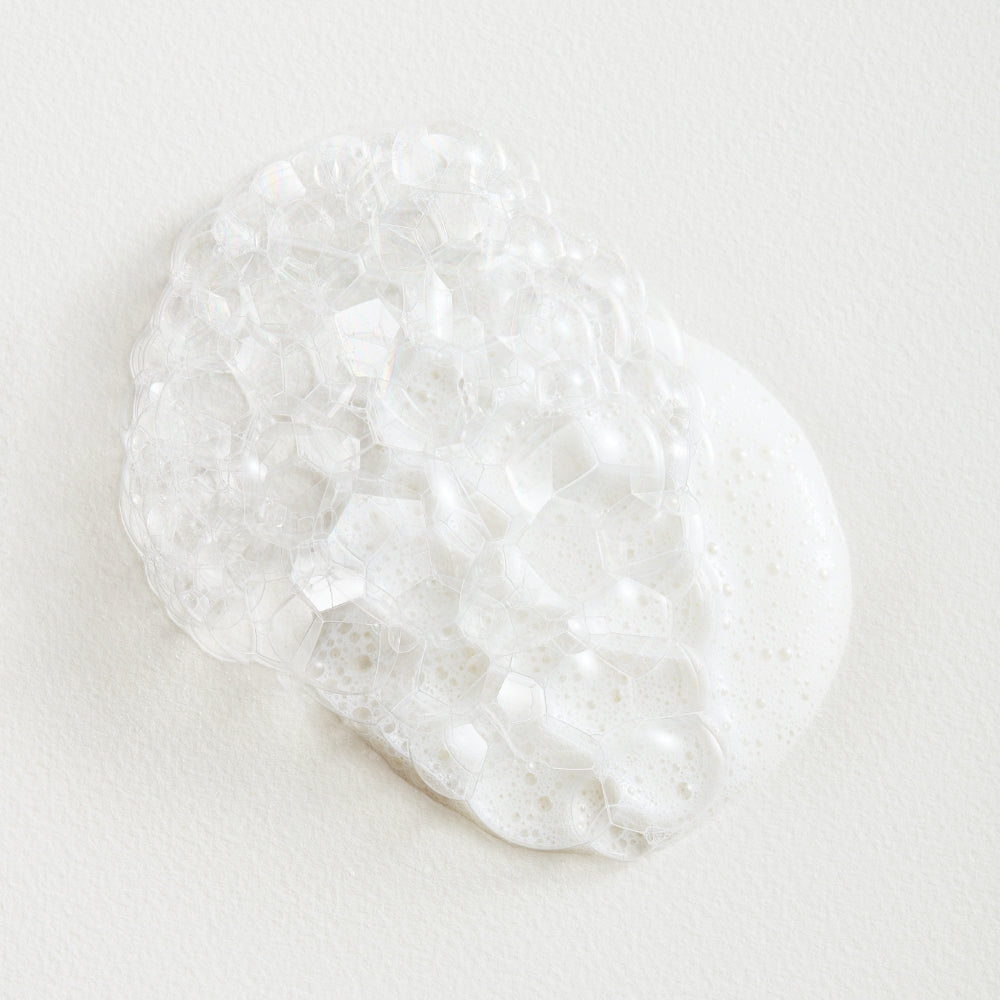 A dollop of foamy soap suds on a white surface.