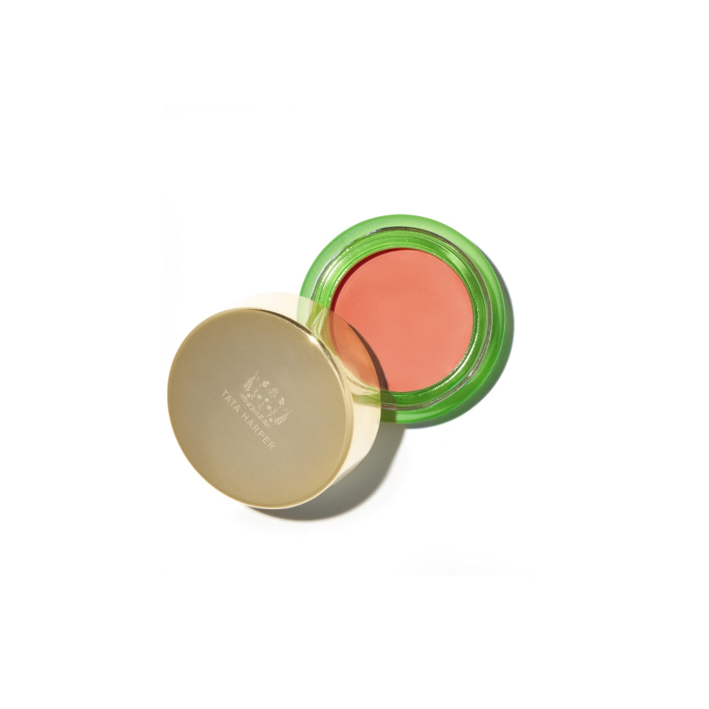Open round compact of coral blush with a metallic gold lid, set on a white background.