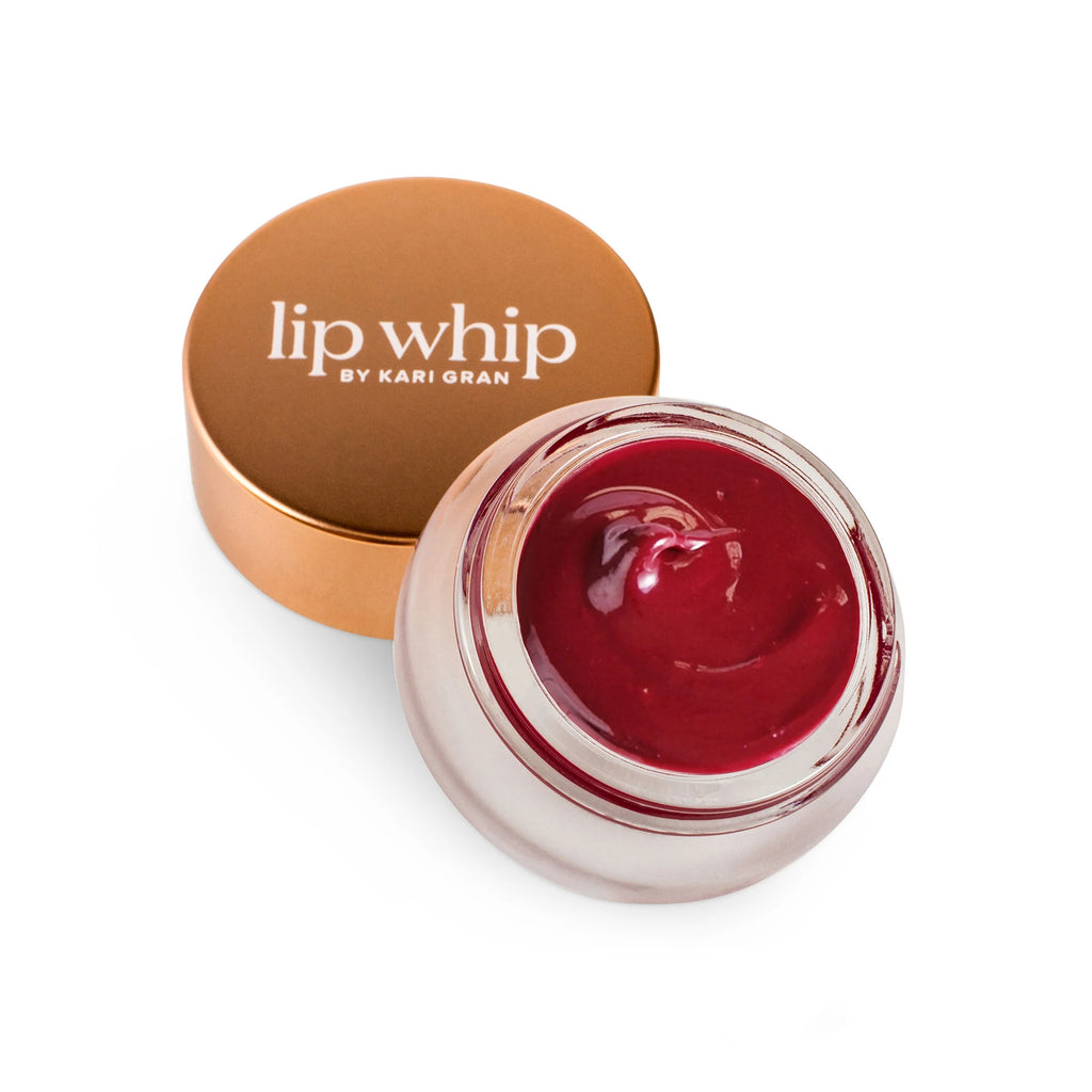 A jar of red-tinted lip whip next to its bronze-colored lid.