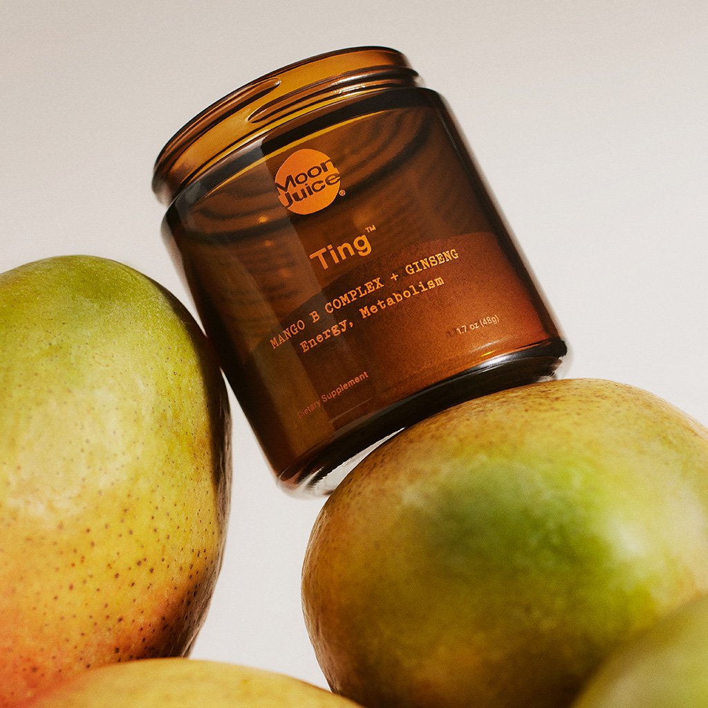 A jar of moon juice ting supplement with mango, amla, and ginseng, placed beside fresh mangoes.