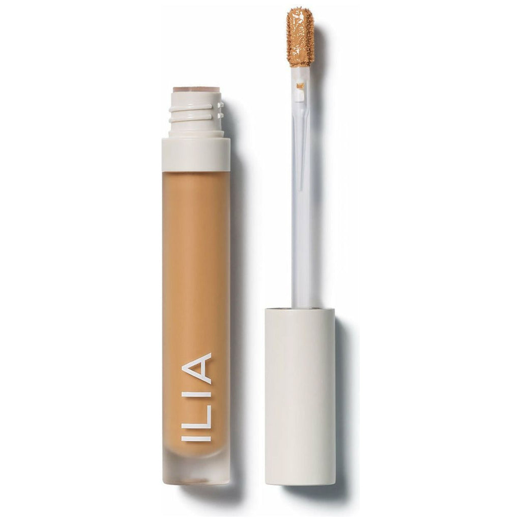 A bottle of ilia concealer next to its applicator wand.