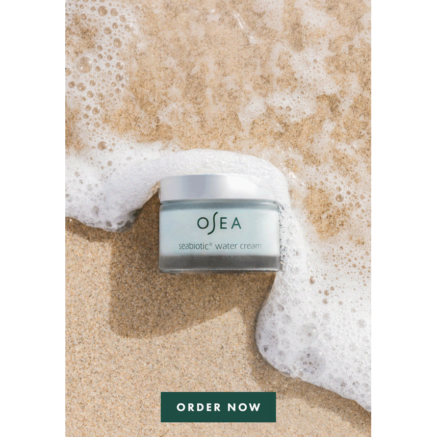 A skincare cream container on a sandy beach with waves approaching it.